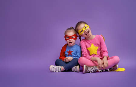 Little children are playing superhero. Kids on the background of bright ultra violet wall. Girl power concept. Yellow, pink, blue, red and purple colors.の写真素材