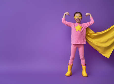 Little child is playing superhero. Kid on the background of bright ultra violet wall. Girl power concept. Yellow, pink and  purple colors.の写真素材