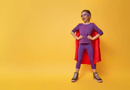 Little child is playing superhero. Kid on the background of bright ultra violet wall. Girl power concept. Yellow, red and  purple colors.の写真素材