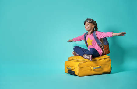 Dreams of travel! Child flying on a suitcase on background of bright blue wall.の写真素材