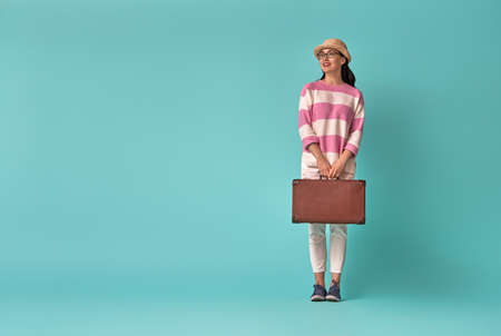 Dreams of travel! Young woman with suitcase on background of bright blue wall.の写真素材
