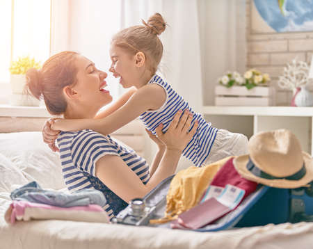 Go on an adventure! Happy family preparing for the journey. Mom and daughter are packing suitcases for the trip.の写真素材