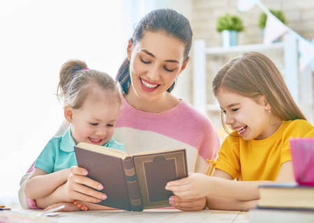 Pretty young mother and her cute daughters are reading a book. Learning to read at home. の写真素材