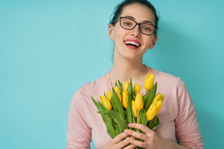 Beautiful young woman in the pink dress with  yellow flowers tulips in hands on light blue background.の写真素材