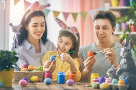 Mother, father and daughter are painting eggs. Happy family are preparing for Easter. Cute little child girl wearing bunny ears.の写真素材