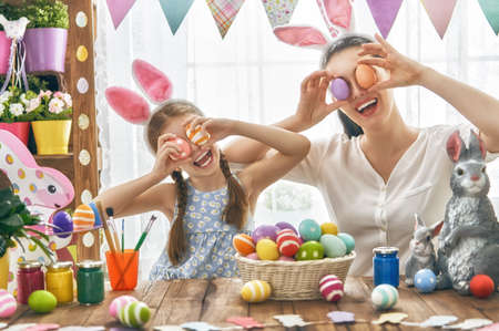 Happy holiday! A mother and her daughter are painting eggs. Family preparing for Easter. Cute little child girl is wearing bunny ears.の写真素材