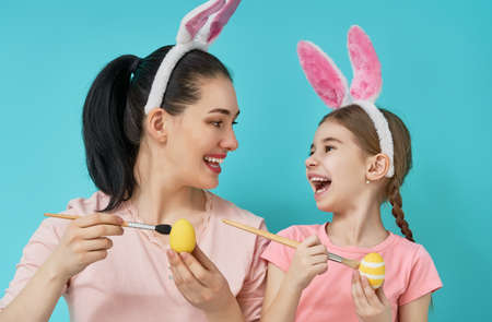 Happy holiday! Mother and her daughter with painting eggs. Family preparing for Easter. Cute little child girl is wearing bunny ears.の写真素材