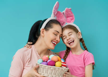 Happy holiday! Mother and her daughter with painting eggs. Family preparing for Easter. Cute little child girl is wearing bunny ears.の写真素材
