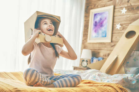 Child girl in an astronaut costume with toy rocket playing and dreaming of becoming a spacemen. Portrait of funny kid in the bedroom.の写真素材