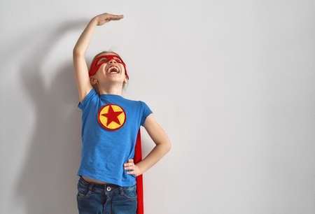 Little child is playing superhero. Kid is measuring the growth on the background of wall. Girl power...