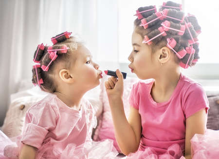 Happy childhood. Two sisters are doing hair and having fun. Children doing makeup sitting on the bed in the bedroom.の写真素材