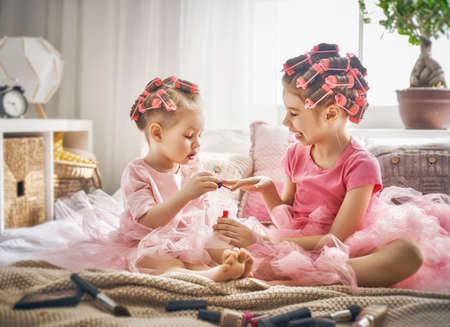 Happy childhood. Two sisters are doing hair and having fun. Children doing makeup sitting on the bed in the bedroom.の写真素材