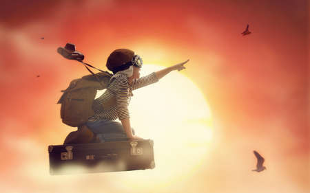 Dreams of travel! Child flying on a suitcase against the backdrop of sunset.の写真素材