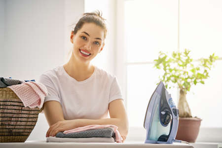 Beautiful young woman is smiling while ironing at home.の写真素材