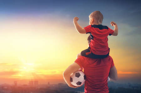 Cute little child dreaming of becoming a soccer player. Boy with man playing football on sunset. Family sport.の写真素材