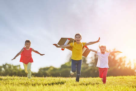 Little children playing astronaut. Girls fleeing and having fun in the park on sunset background. Kid in an astronaut costume dreaming of becoming a spaceman. Family games outdoors.の写真素材