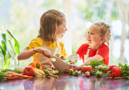 Healthy food at home. Happy family in the kitchen. Two cute funny children are preparing the vegetables.の写真素材