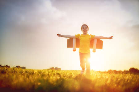 Little girl playing astronaut. Child fleeing on the background of sunset sky. Kid dreaming of becoming a spaceman.の写真素材