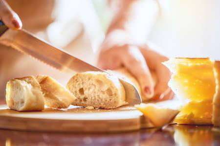 Hands of person cutting bread and cheese on wooden table.の写真素材
