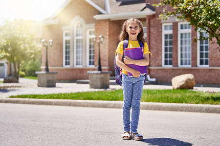 Pupil of primary school with book in hand. Girl with backpack near building outdoors. Beginning of lessons. First day of fall.の写真素材