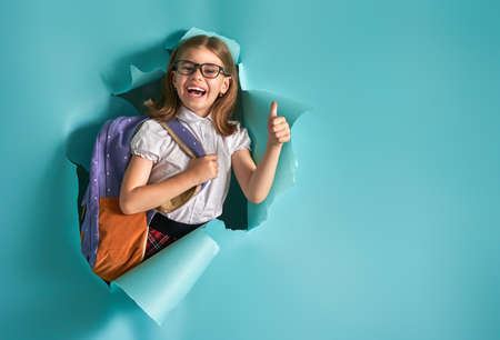 Back to school and happy time! Cute industrious child is breaking through color paper wall. Kid with...
