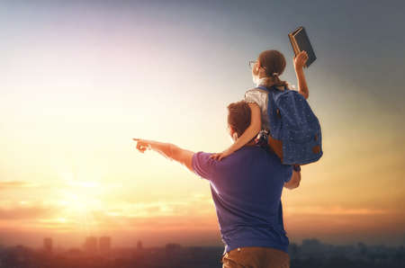 Parent and pupil of primary school on sunset background. Man and girl with backpack behind the back. Beginning of lessons. First day of fall.の写真素材