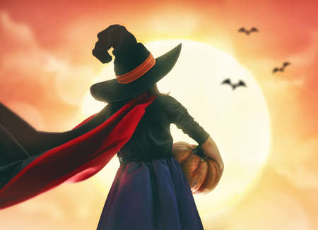 Happy Halloween! Cute little witch with pumpkin. Child girl outdoors.