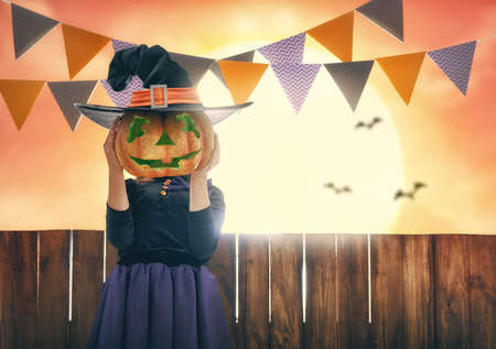 Happy Halloween! Cute little witch with pumpkin. Beautiful young child girl in costume on sunset background.の写真素材