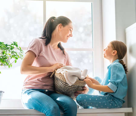 Beautiful young woman and child girl little helper are having fun and smiling while doing laundry at home.の写真素材