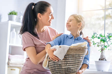 Beautiful young woman and child girl little helper are having fun and smiling while doing laundry at home.の写真素材
