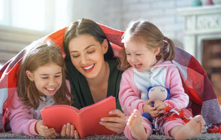 Winter portrait of happy loving family. Pretty young mother reading a book to her daughters at home.の写真素材