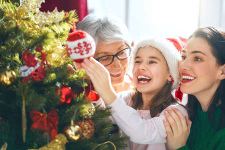 Merry Christmas and Happy Holidays! Grandma, mom and daughter decorate the tree indoors. The morning...