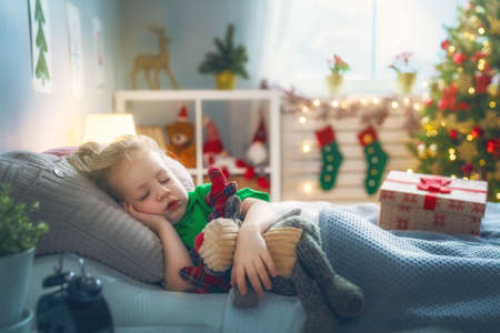 Merry Christmas and Happy Holiday! Cute little child girl sleeping in the bed near tree at home.の写真素材