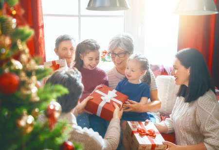 Merry Christmas and Happy Holidays! Grandma, grandpa, mum, dad and child exchanging gifts. Parents and daughter having fun near tree indoors. Loving family with presents in room.の写真素材