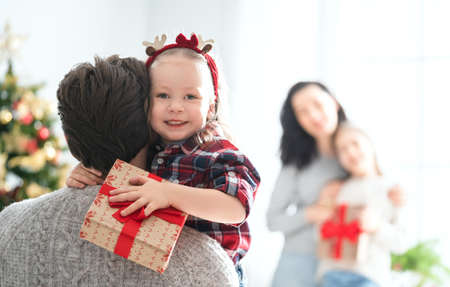 Merry Christmas and Happy Holidays! Mum, dad and children exchanging gifts. Parents and daughters having fun near tree indoors. Loving family with presents in room.の写真素材