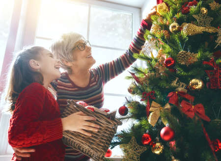 Merry Christmas and Happy Holidays! Grandma and child decorate the tree indoors. The morning before Xmas. Portrait loving family close up.の写真素材