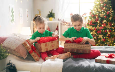 Merry Christmas and Happy Holidays! Cheerful cute childrens girls opening gifts on the bed. Kids wearing pajamas having fun near tree in the morning. Loving family with presents in room.の写真素材