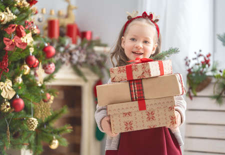 Merry Christmas and Happy Holiday! Cute little child girl with present gift boxes near tree at home.の写真素材