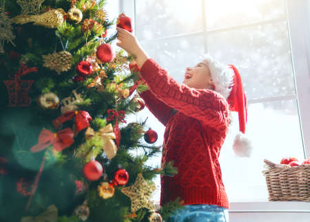 Merry Christmas and Happy Holidays! Cute little child girl is decorating the tree indoors. The morning before Xmas. Portrait kid close up.の写真素材