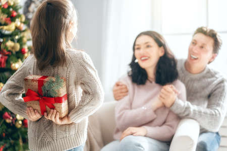 Merry Christmas and Happy Holidays! Mum, dad and child exchanging gifts. Parents and daughter having fun near tree indoors. Loving family with presents in room.の写真素材