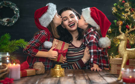 Merry Christmas and Happy Holiday! Mom and daughters with gifts near the tree at home.