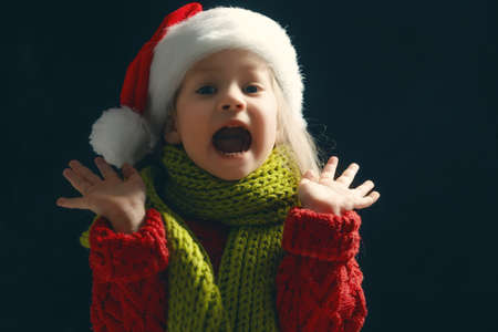 Happy child girl in Santa hat on dark background. Little kid amazed at Christmas.の写真素材