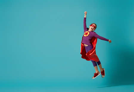 Little child is playing superhero. Kid on the background of bright blue wall. Girl power concept.