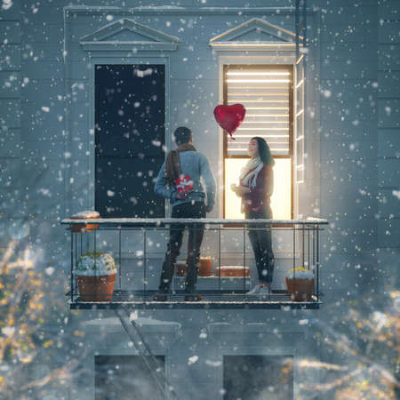 Romantic couple holding Valentines gift standing on the balcony on a date.