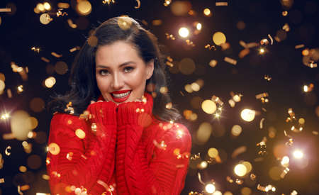 Smiling beautiful young woman in red sweater posing on black background.