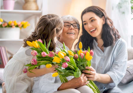 Happy women's day! Child daughter is congratulating mom and granny giving them flowers tulips....