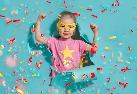 Little child playing superhero. Kid on the background of bright blue wall. Girl power concept. Yellow, pink and  turquoise colors.の写真素材