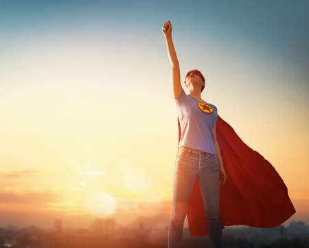 Joyful beautiful young woman in superhero costume posing on sunset background.の写真素材