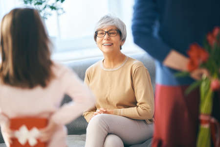 Happy women's day! Child daughter is congratulating mom and granny giving them flowers tulips. Grandma, mum and girl smiling and hugging. Family holiday and togetherness.の写真素材