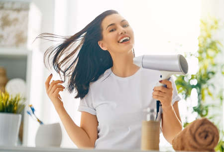 Happy young woman is blowing dry hair in the bathroom.